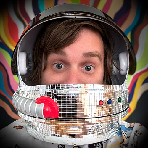 Brad Frost wearing an astronaut helmet with a mirrored disco-ball faceplate, against a colorful painted mural background